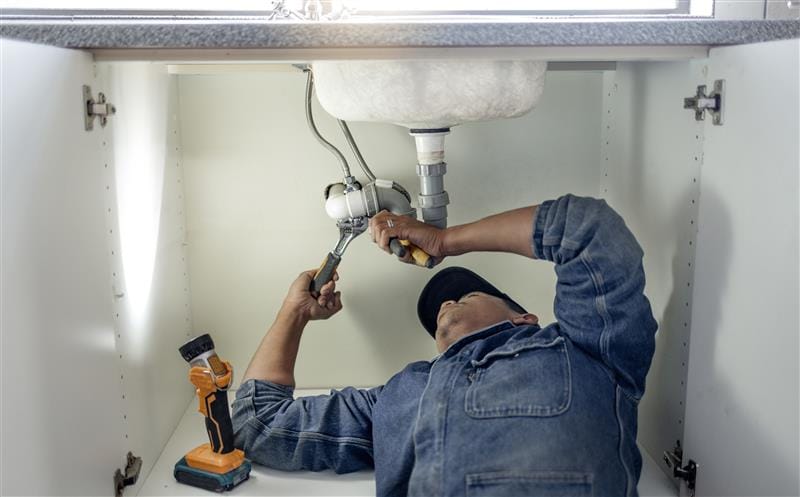 Plumber repairing pipes beneath a bathroom sink in Fort Walton Beach