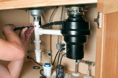 Plumber repairing a garbage disposal beneath a kitchen sink in Fort Walton Beach