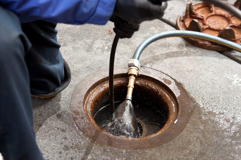 Plumber hydro jetting a sewer line through a manhole in Fort Walton Beach