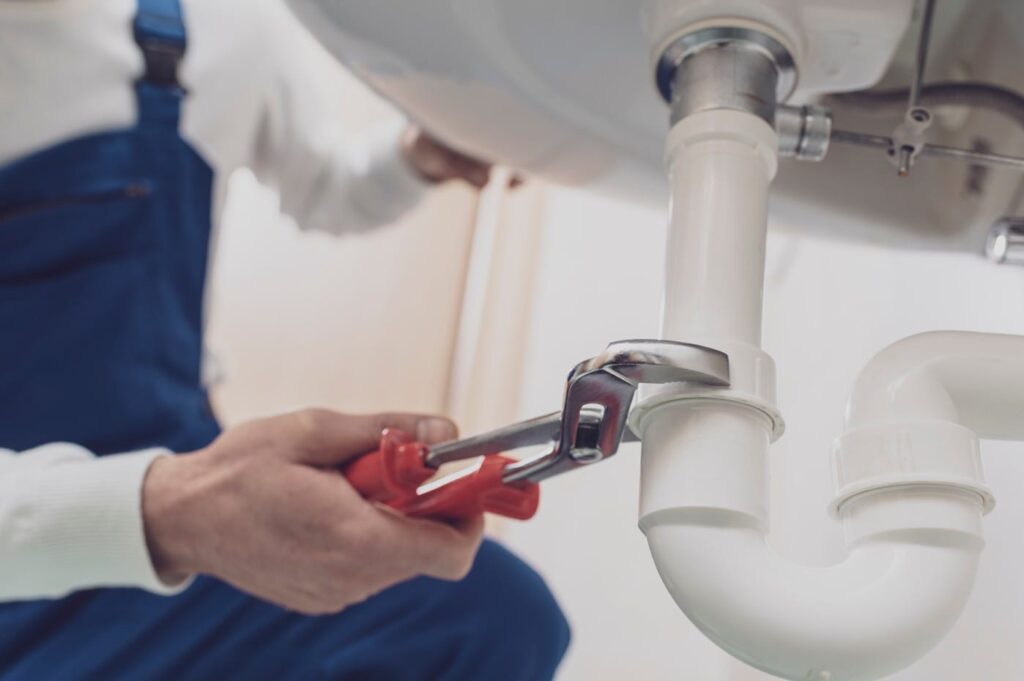 Plumber repairing a white drain pipe beneath a sink in Fort Walton Beach