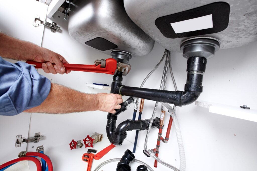 Plumber repairing drain pipes beneath a kitchen sink in Fort Walton Beach